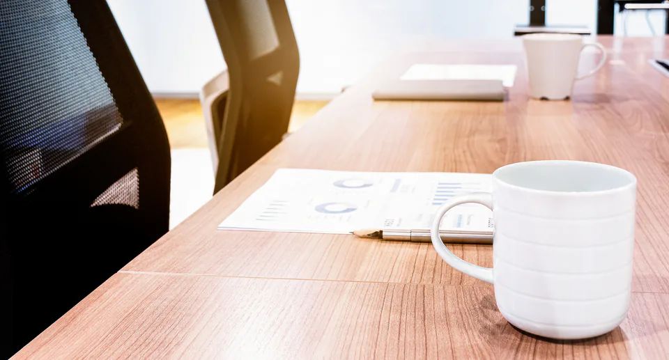 Coffee mug and paperwork on a meeting table beside empty office chairs.
